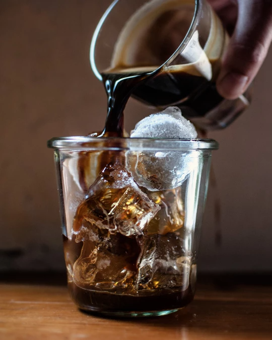 ES-persona-vertiendo-cafe-caliente-en-un-vaso-con-hielo-vertical